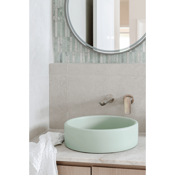 Close-up of mint green basin with Kit Kat Paradiso Green Finger Mosaic tiles on the wall and brushed brass tapware.