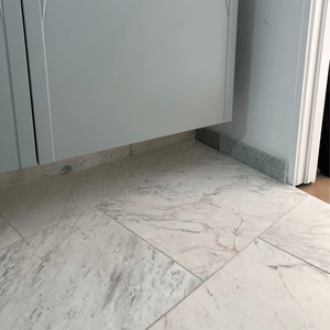 Close-up of Greek Volakas Marble flooring with soft grey and beige veining beneath a floating cabinet.