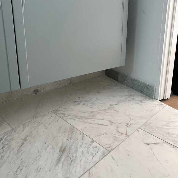 Close-up of Greek Volakas Marble flooring with soft grey and beige veining beneath a floating cabinet.
