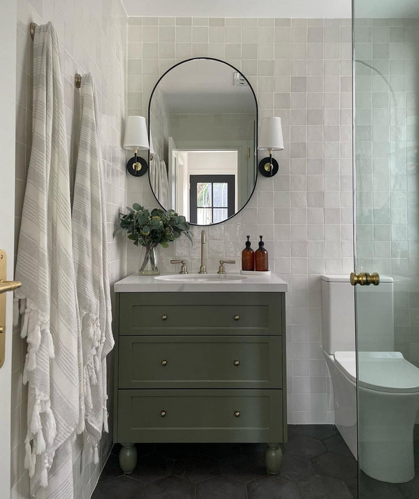 modern-traditional bathroom design with soft green ceramic tiles on the walls and green cupboard. Two white towels hand on the left side.