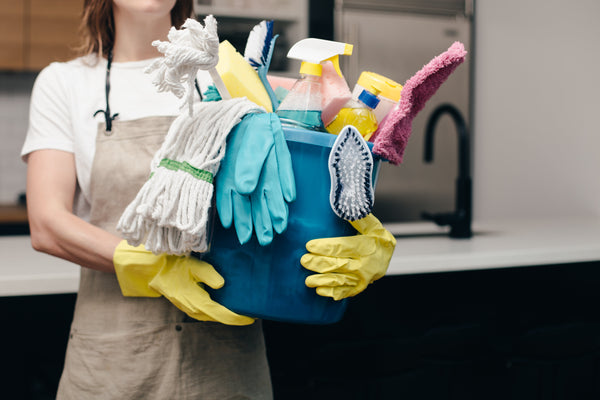 woman holding cleaning tools in a bucket. She is wearing gloves.