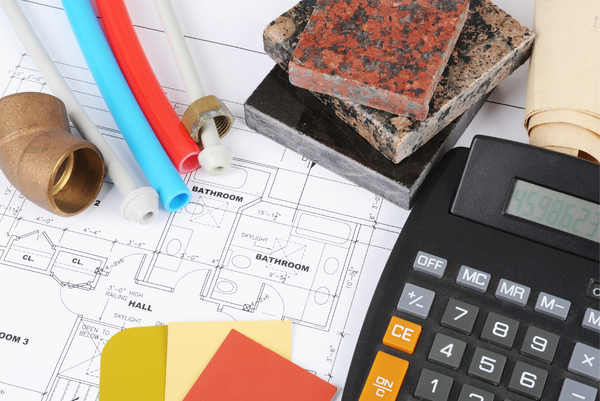 a calculator, swatches of colour cards and tile samples laid out over a home building plan.