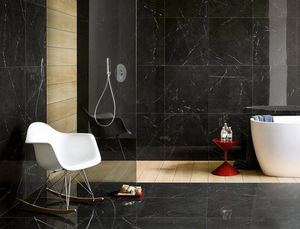 bathroom with dark pietra grey marble covering the floor and walls. There is a white bathtub and chair in the image.